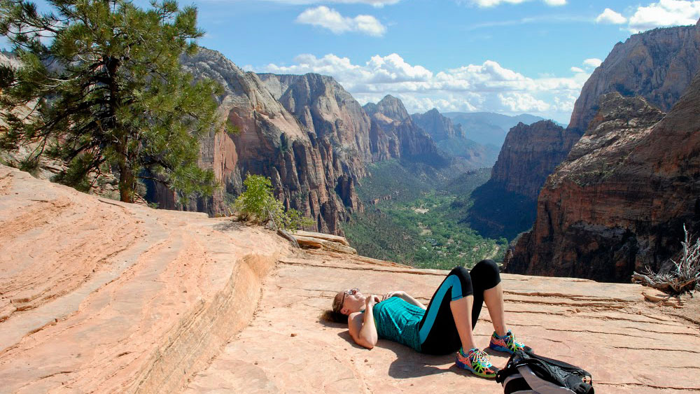 A woman relaxes on a rocky ledge with a scenic mountain view.
